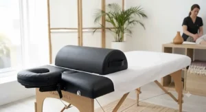 Portable massage table equipped with a matching black knee bolster and face cradle pillow.